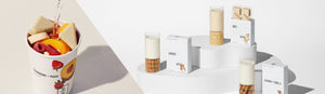 Mylk All Collections Header for Desktop. Features an evergreen image of all three Mylk SKUs (Almond, Oat, Almond + Vanilla) with packaging and a use-case image featuring Strawberry + Peach Smoothie with two Mylk wedges and water being poured into the cup.