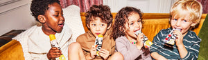 Four small children eating pops on a couch.