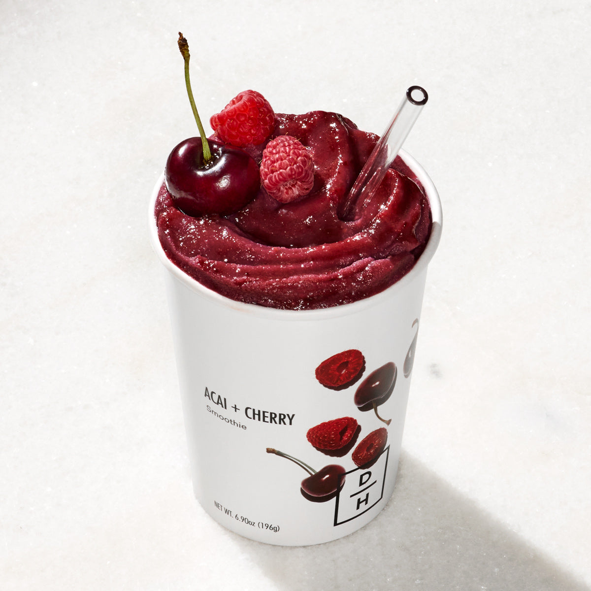 Daily Harvest Acai + Cherry Smoothie prepared with a raspberry and cherry garnish with a straw.