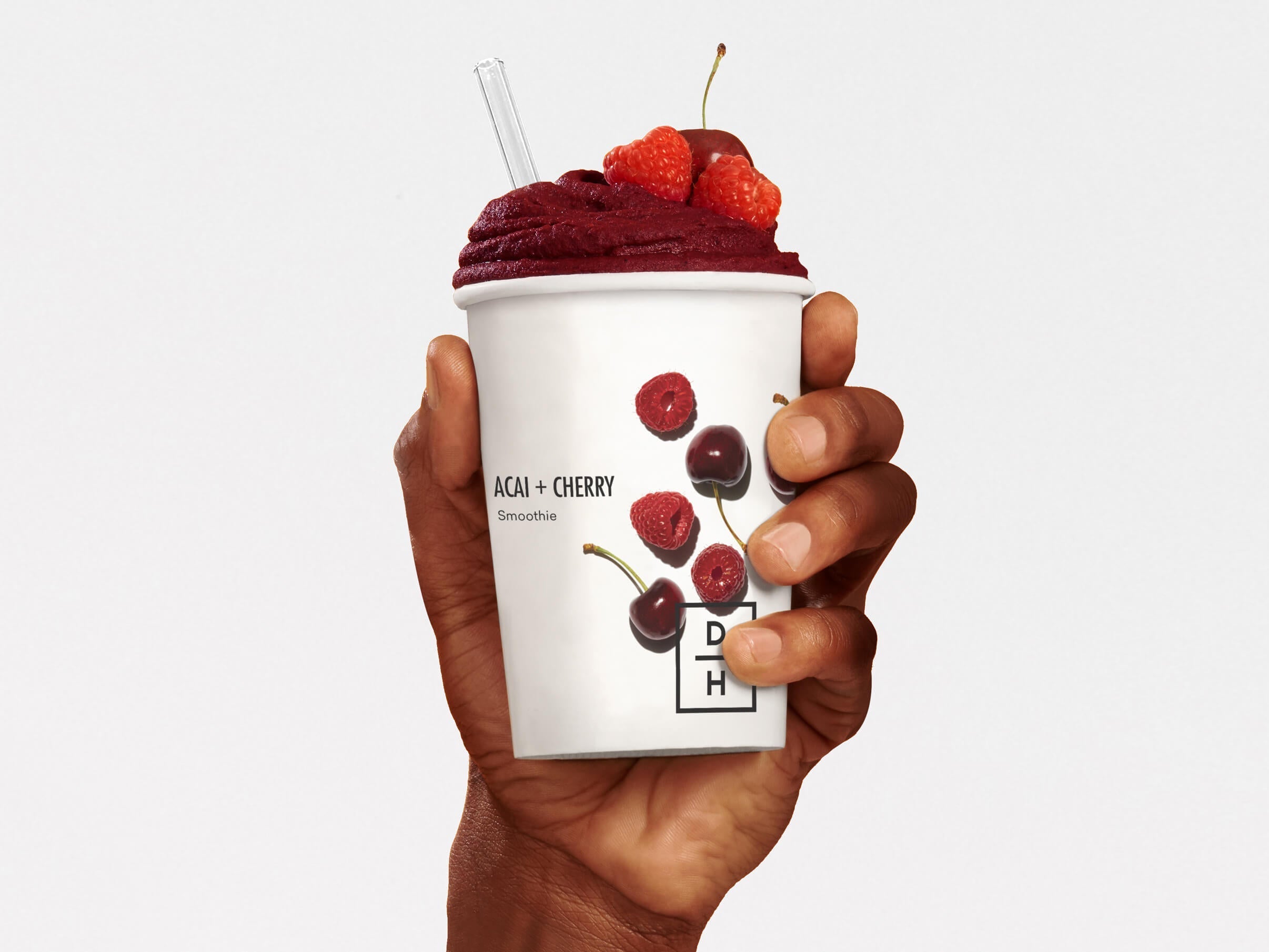 A hand holding a prepared Daily Harvest Acai + Cherry Smoothie with garnish.