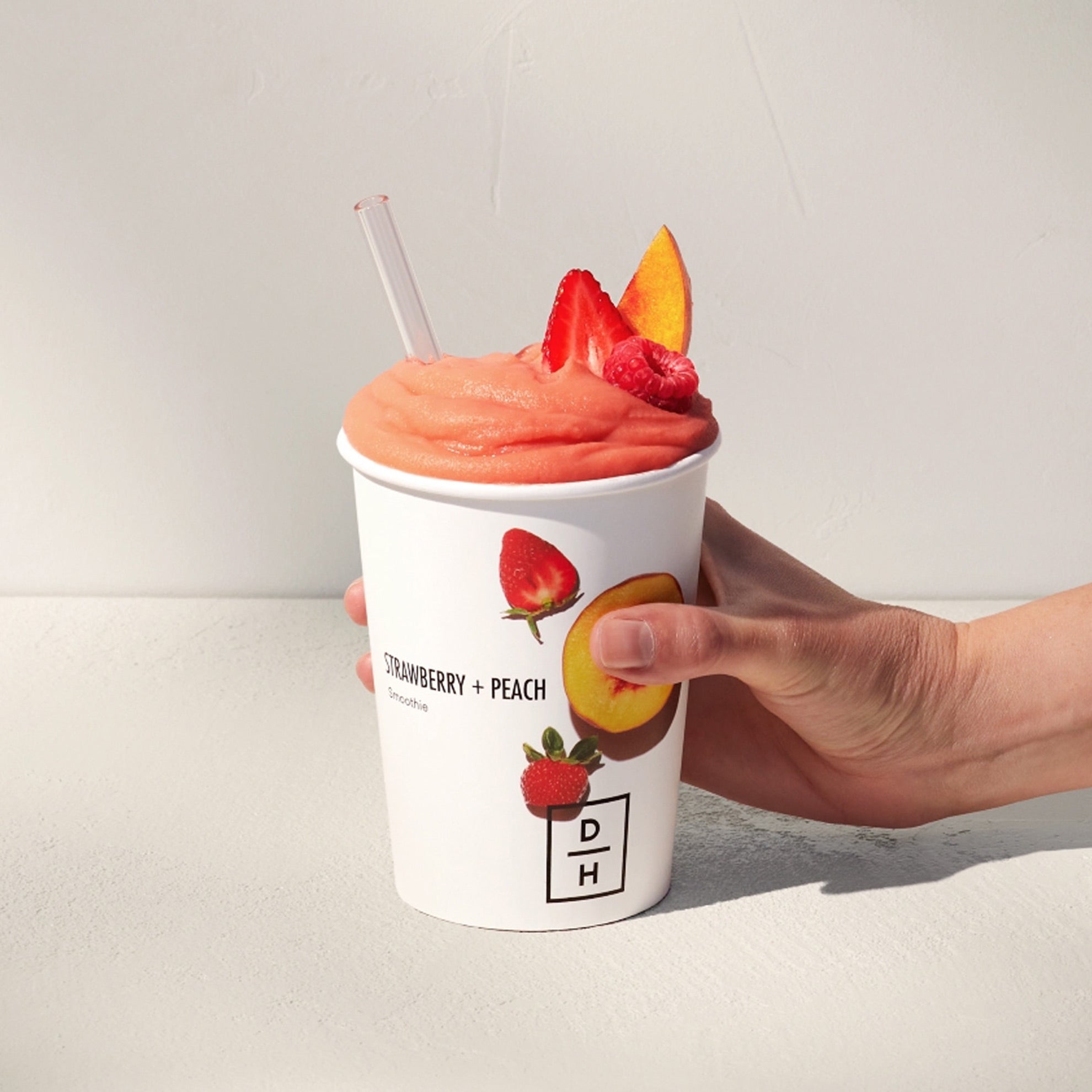 Daily Harvest Strawberry + Peach Smoothie prepared in a cup with strawberry, peach and raspberry garnish.