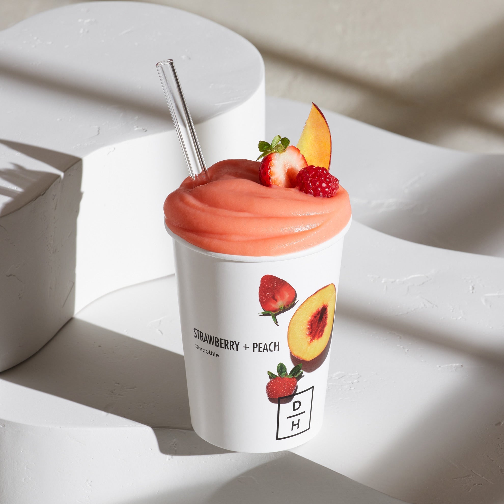 Daily Harvest Strawberry + Peach Smoothie prepared in a cup with strawberry, peach and raspberry garnish.