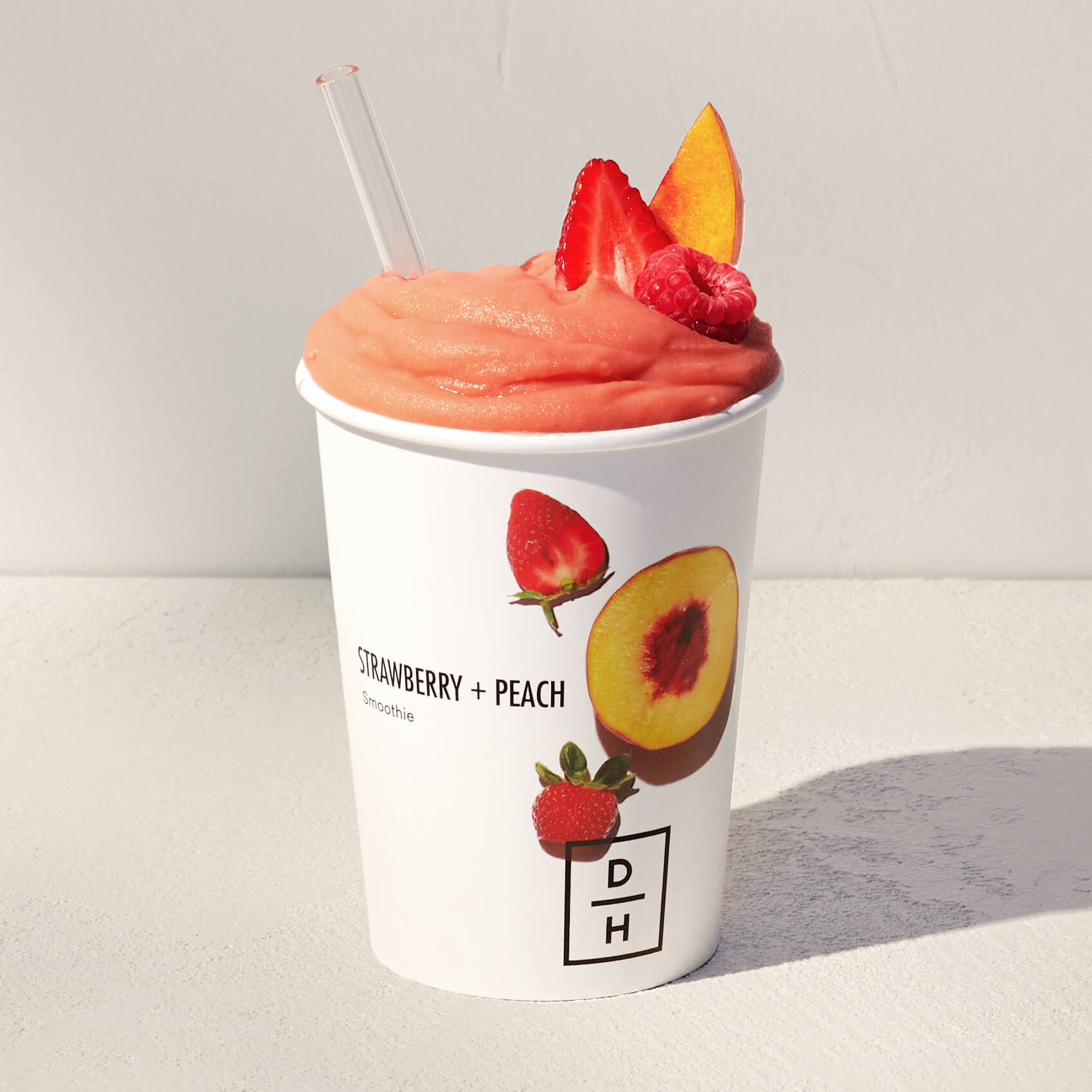 Daily Harvest Strawberry + Peach Smoothie prepared in a cup with strawberry, peach and raspberry garnish.