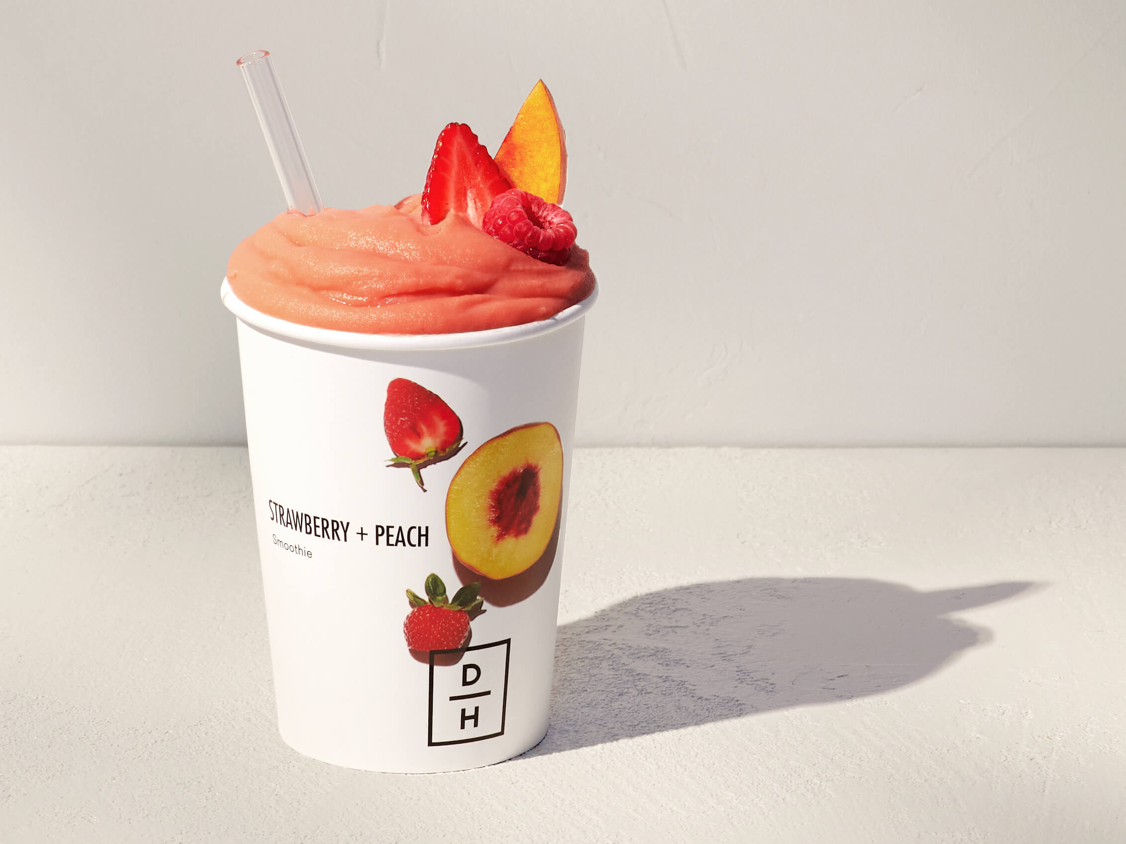 Daily Harvest Strawberry + Peach Smoothie prepared in a cup with strawberry, peach and raspberry garnish.