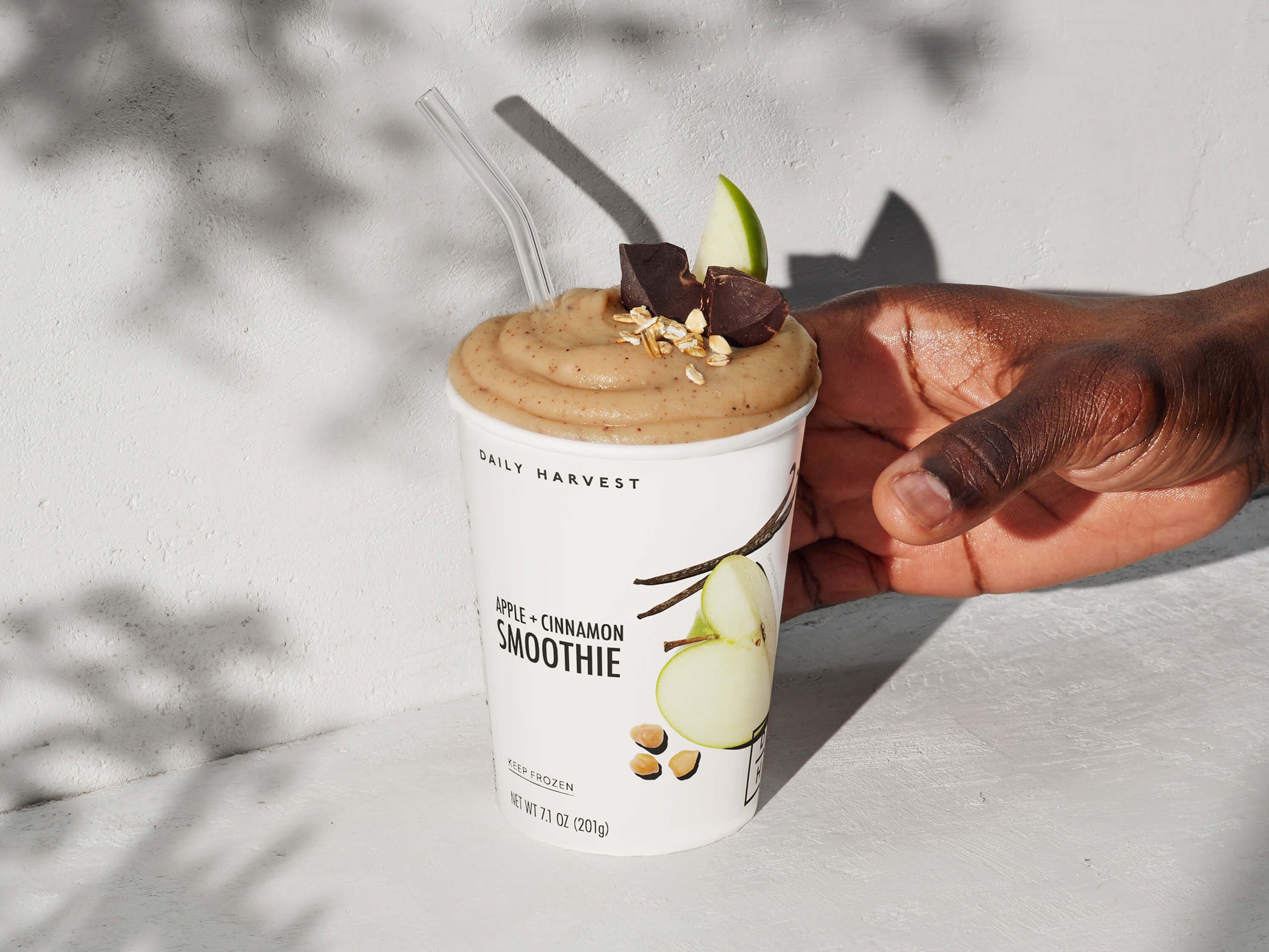 A hand reaching toward an Apple + Cinnamon Smoothie garnished with an apple and cacao. 