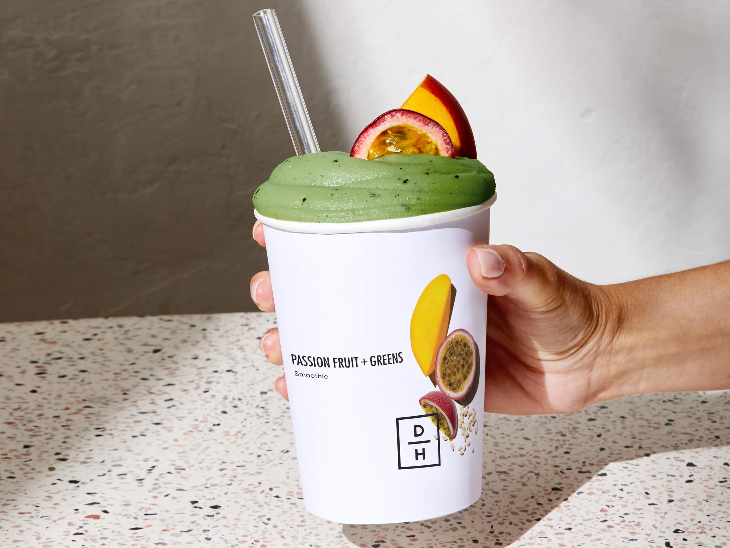 A hand holding a prepared Passion Fruit + Greens Smoothie 