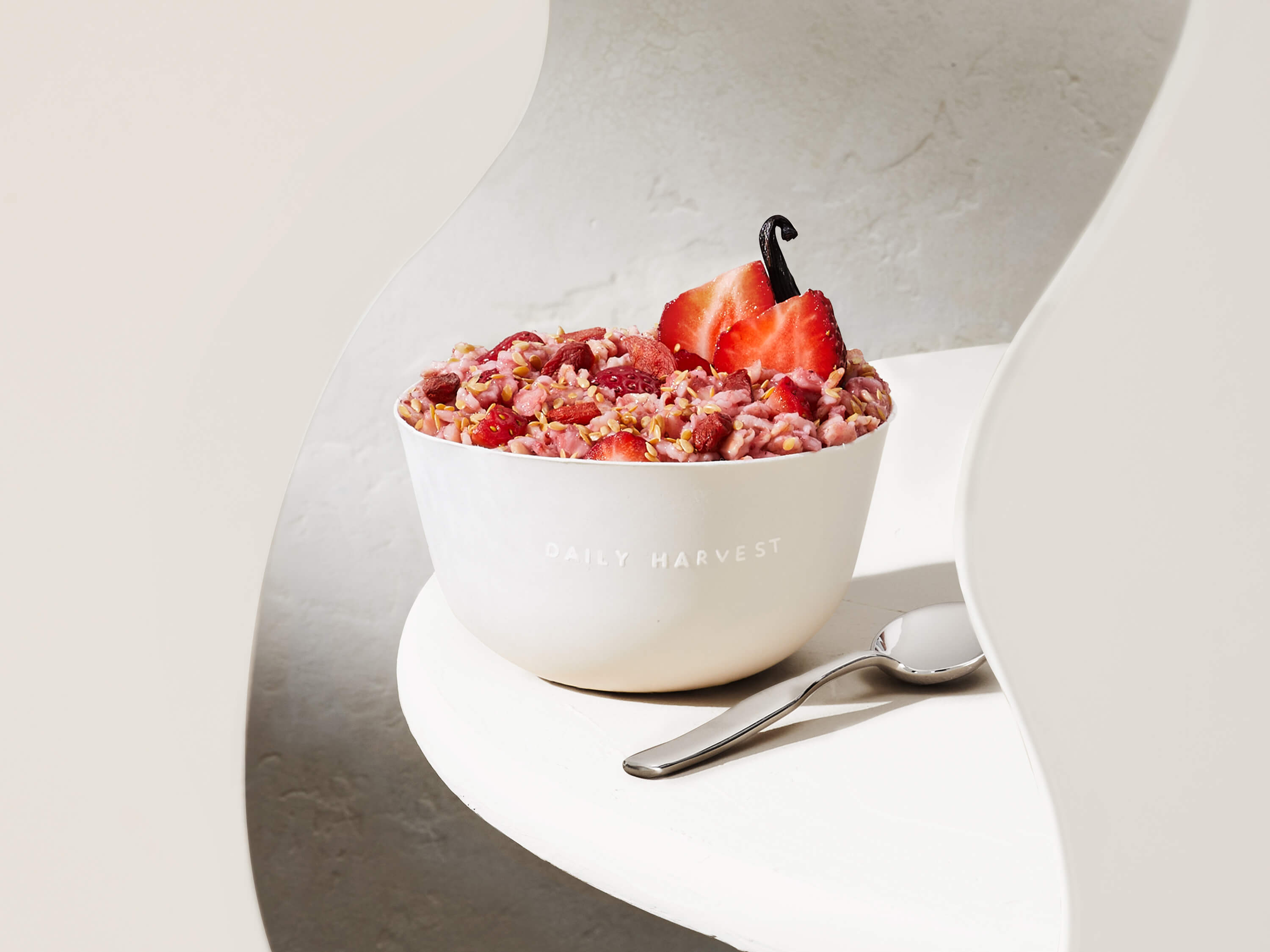 Lifestyle image of Daily Harvest Strawberry + Goji Berry Oat Bowl prepared in a bowl with a spoon and two strawberry halves on the side.