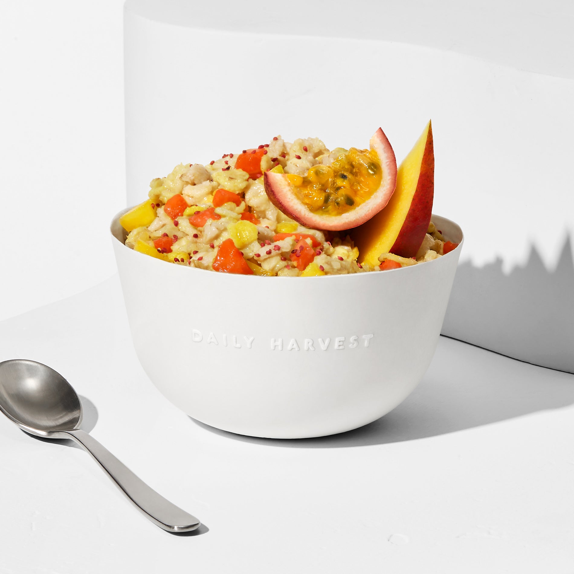 Prepared Pineapple + Passion Fruit Forager Bowl in a white bowl with passion fruit and mango garnish next to a spoon.