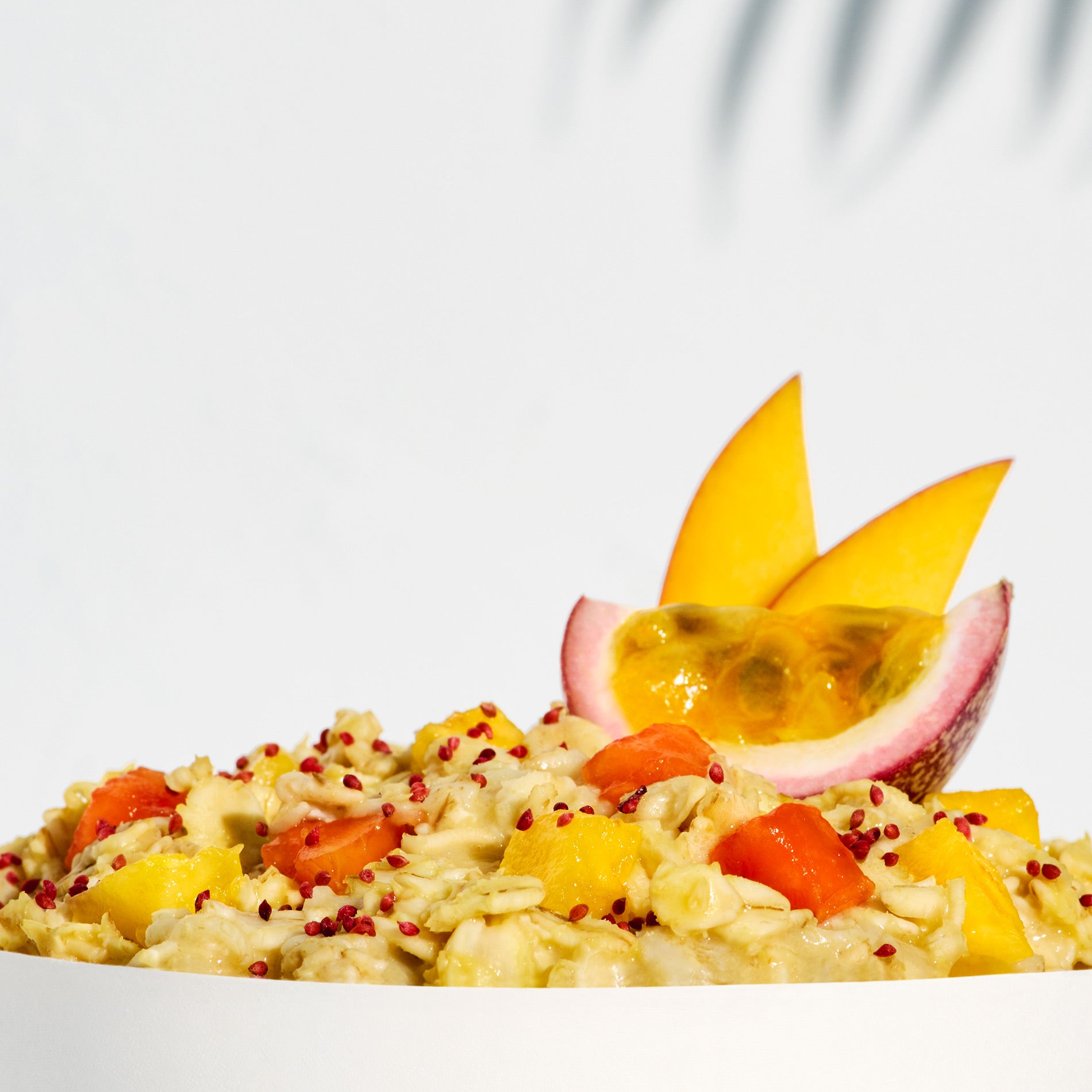 A close-up of a prepared Pineapple + Passion Fruit Forager Bowl in a white bowl with passion fruit and mango garnish.