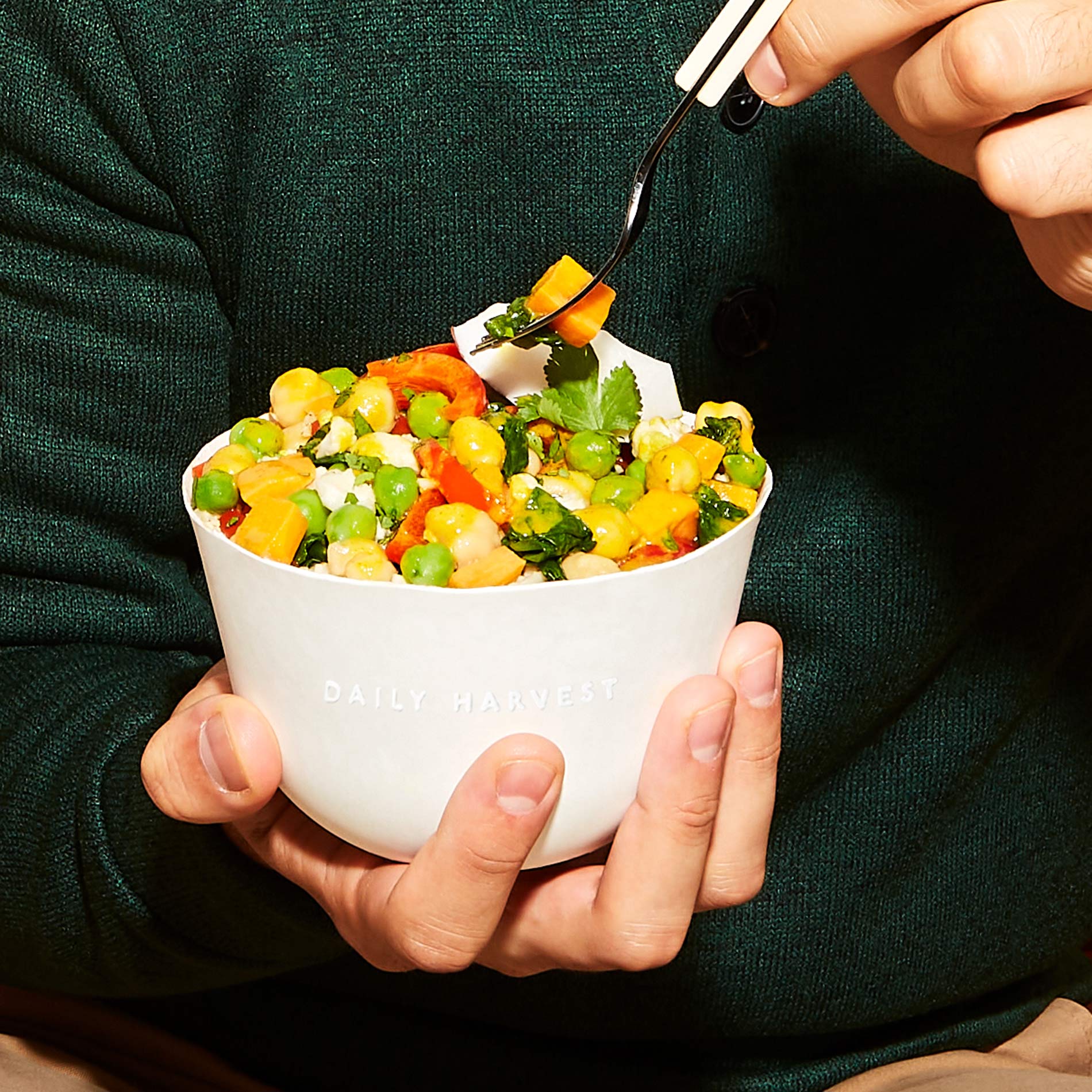 A hand holding a Chickpea + Coconut Curry Harvest Bowl and dipping into it with a fork.