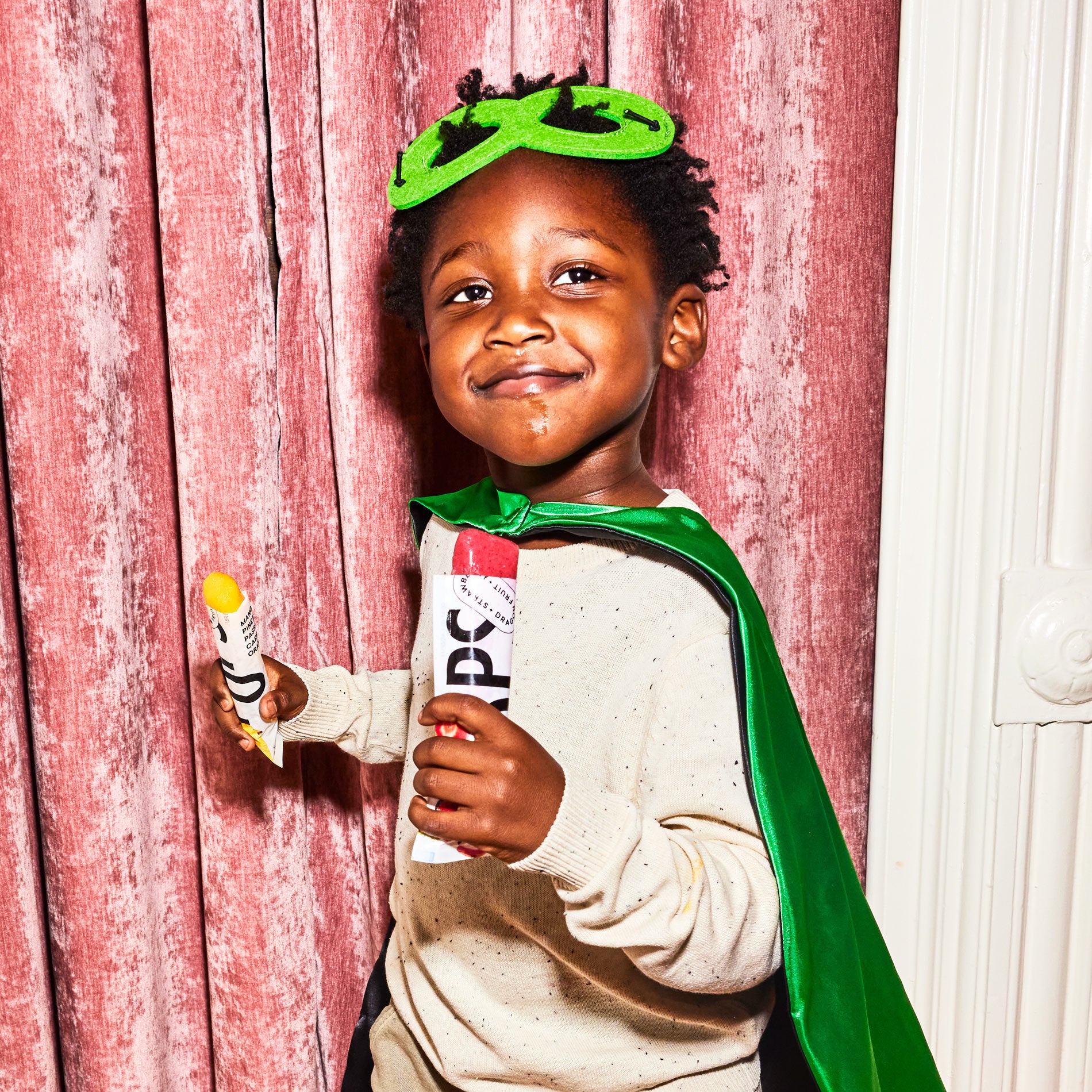 A child in a superhero costume holding two open Pops.