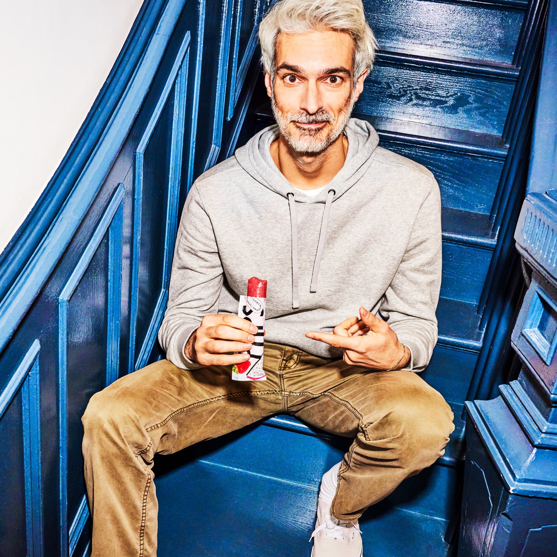 A person sitting on blue stairs holding a Strawberry + Dragon Fruit Pop.