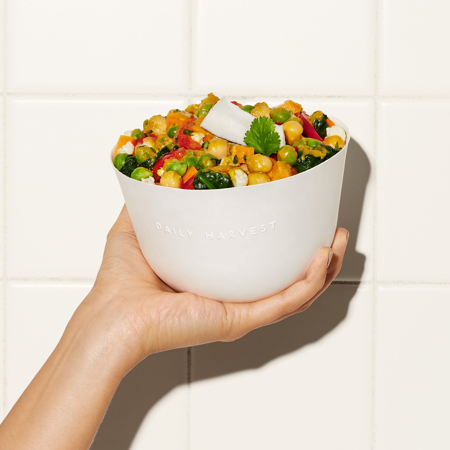 A hand holding a bowl of Chickpea + Coconut Curry