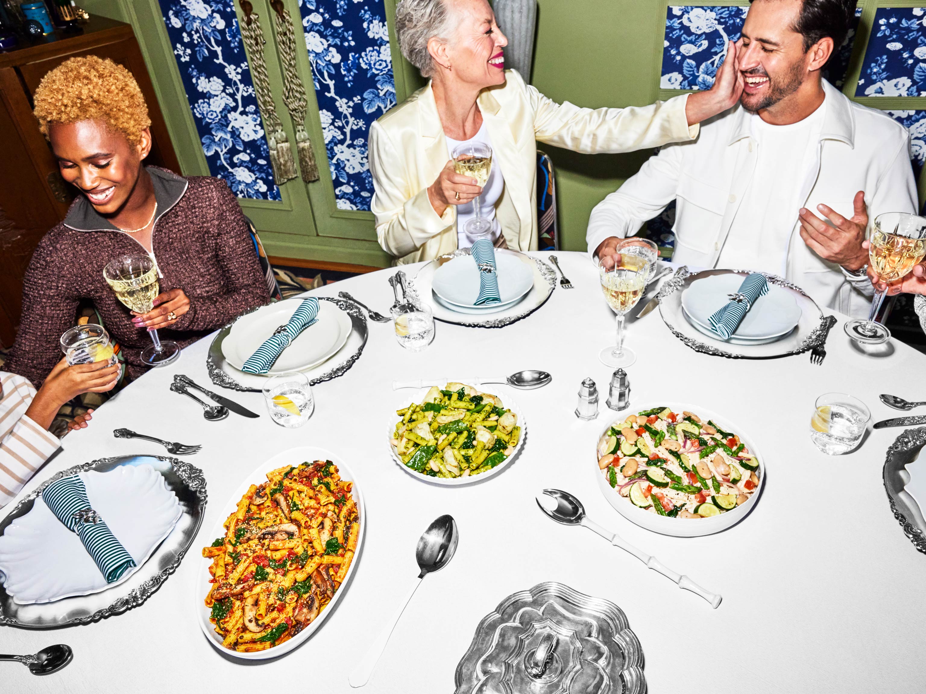 8. Three people at a table with place settings and bowls of prepared Daily Harvest pasta on it.