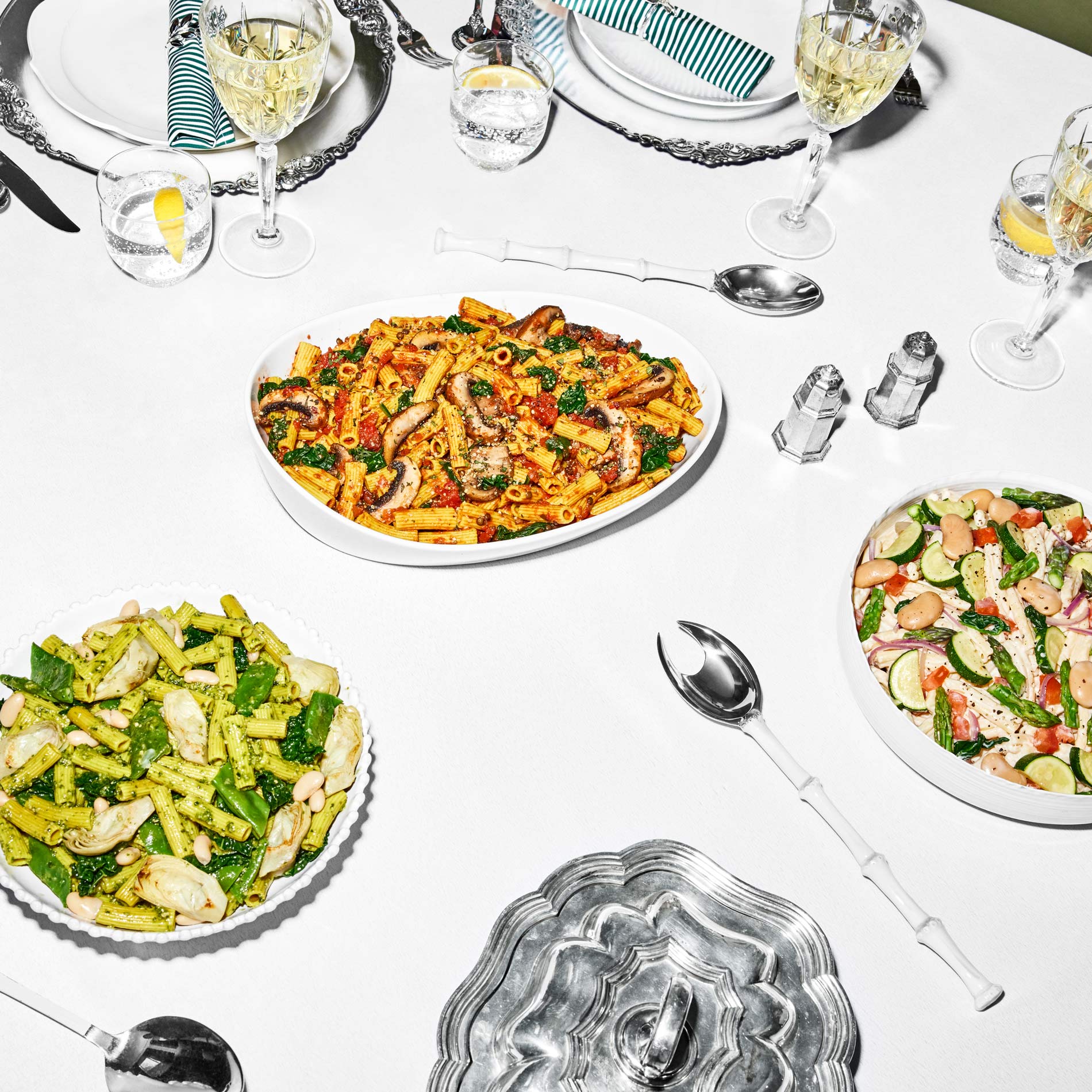 9. Daily Harvest’s White Bean + Spinach Pesto Pasta, Tomato Basil + Portobello Bolognese, and Zucchini + Gigante Bean Primavera prepared in serving dishes on a table with place settings.