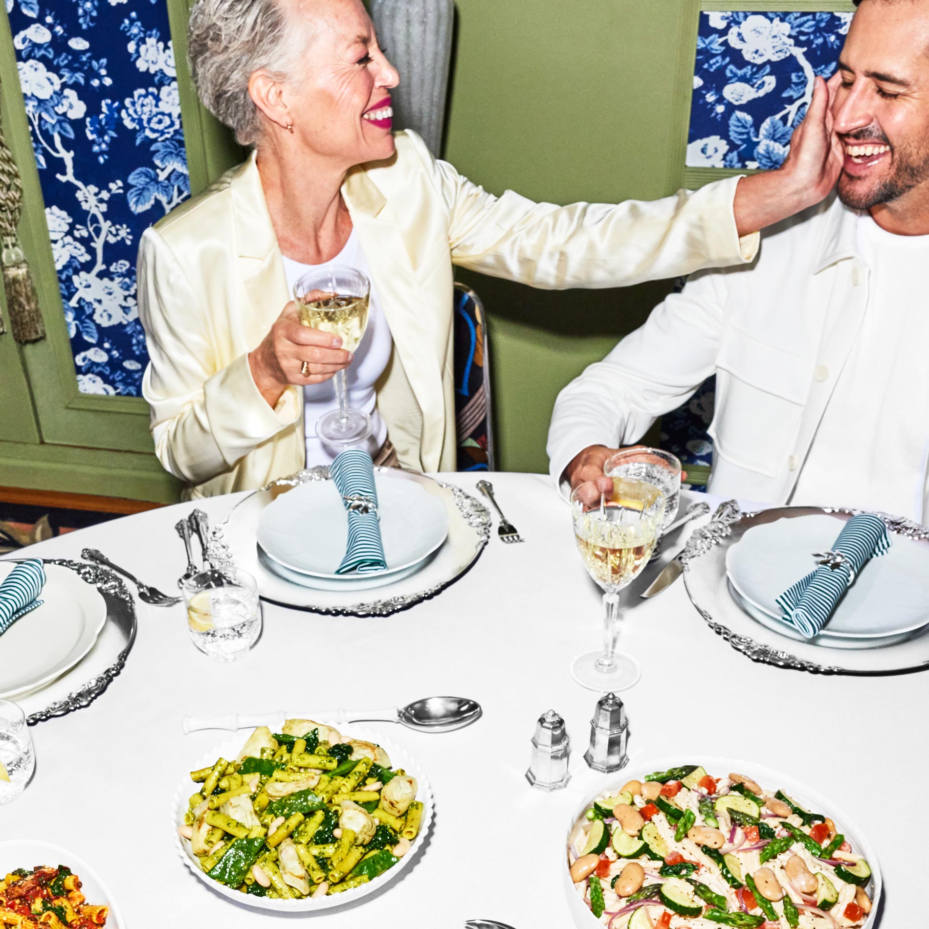 Two people at a table with place settings and bowls of prepared Daily Harvest pasta on it.