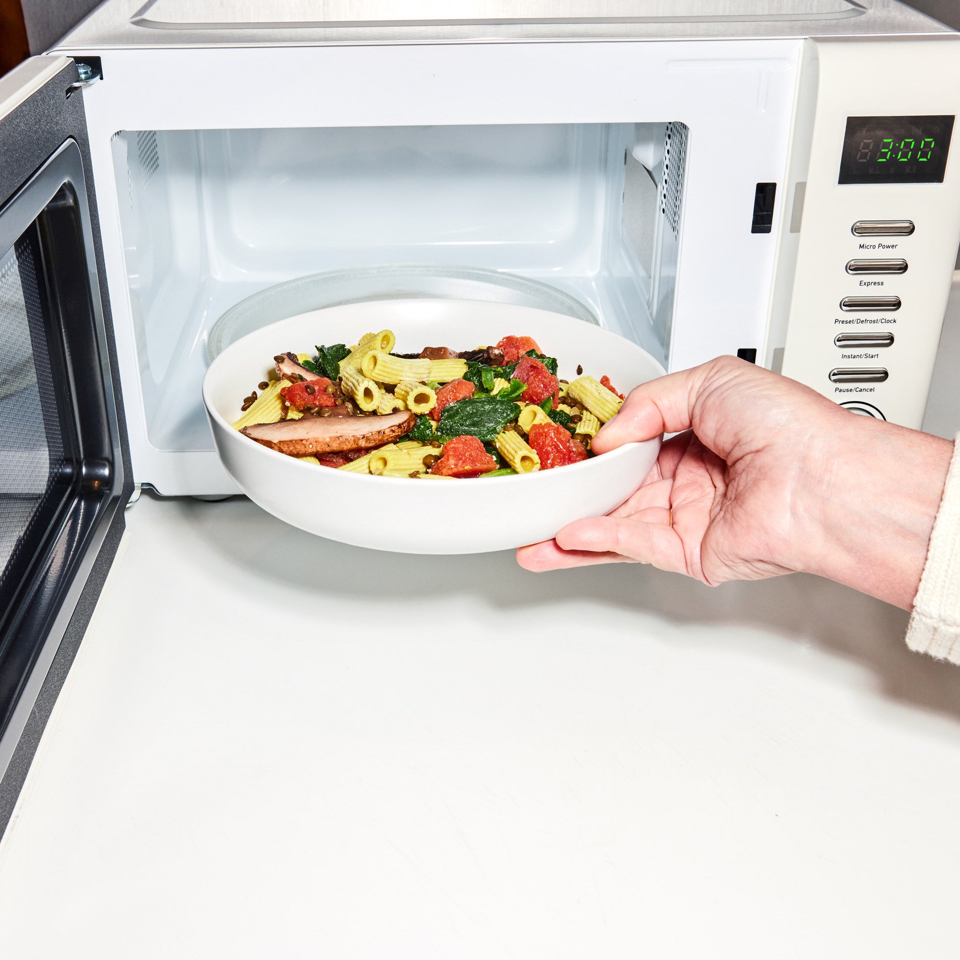 A hand putting frozen Daily Harvest pasta into a microwave in a microwave-safe dish.