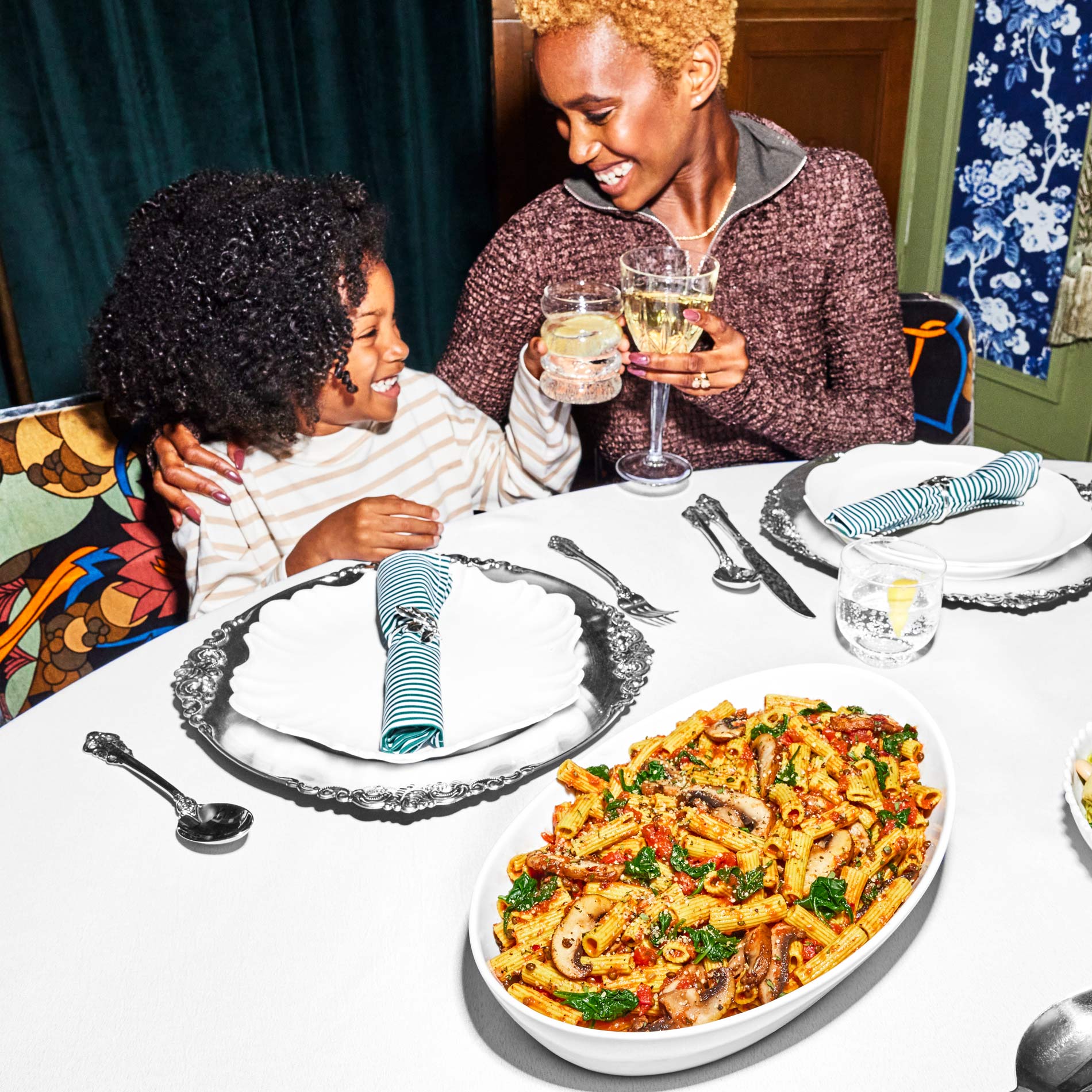 Two people at a table with place settings and a bowl of prepared Tomato Basil + Portobello Bolognese Daily Harvest pasta on it.