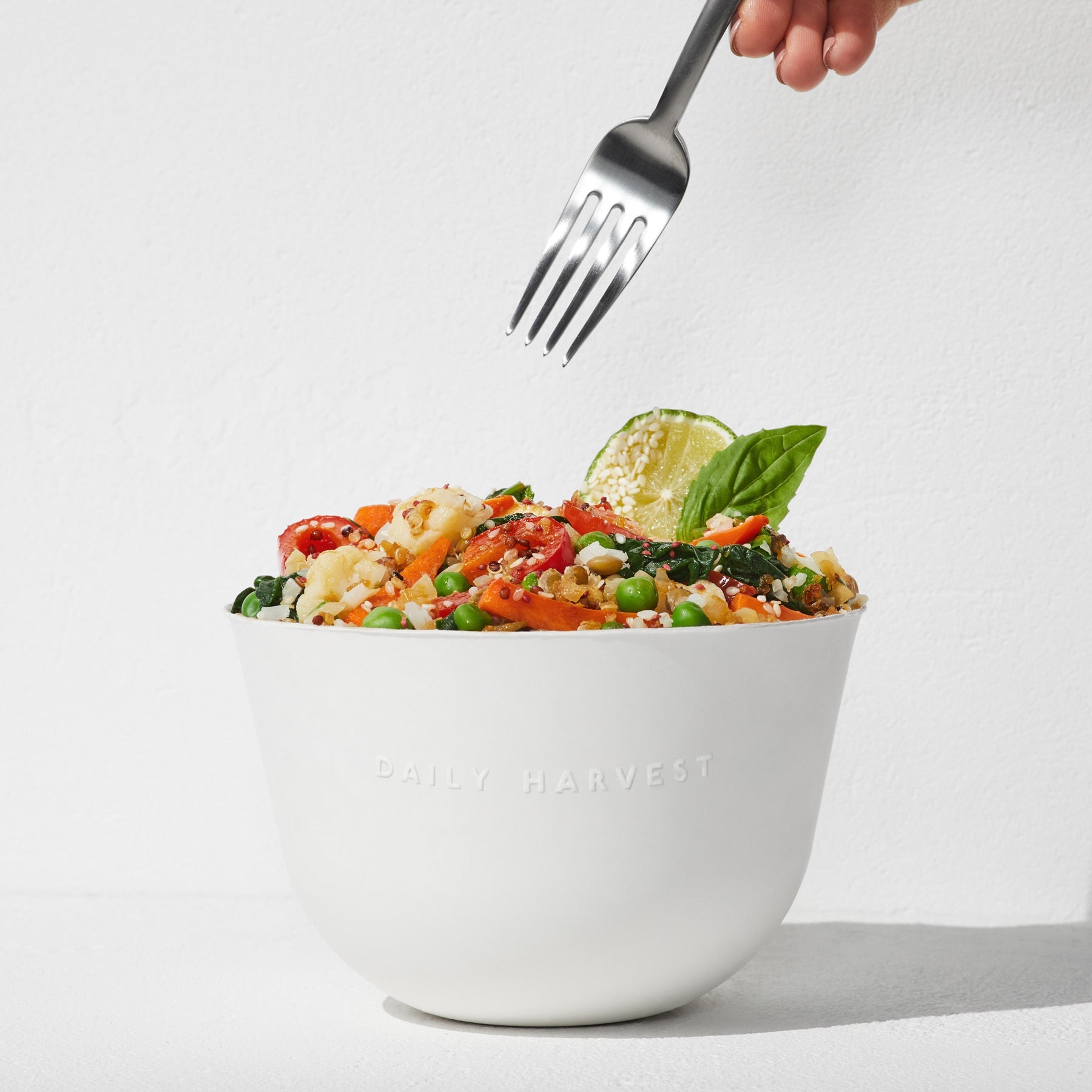 A hand holding a fork over a prepared Quinoa + Makrut Lime Harvest Bake in a large white bowl.