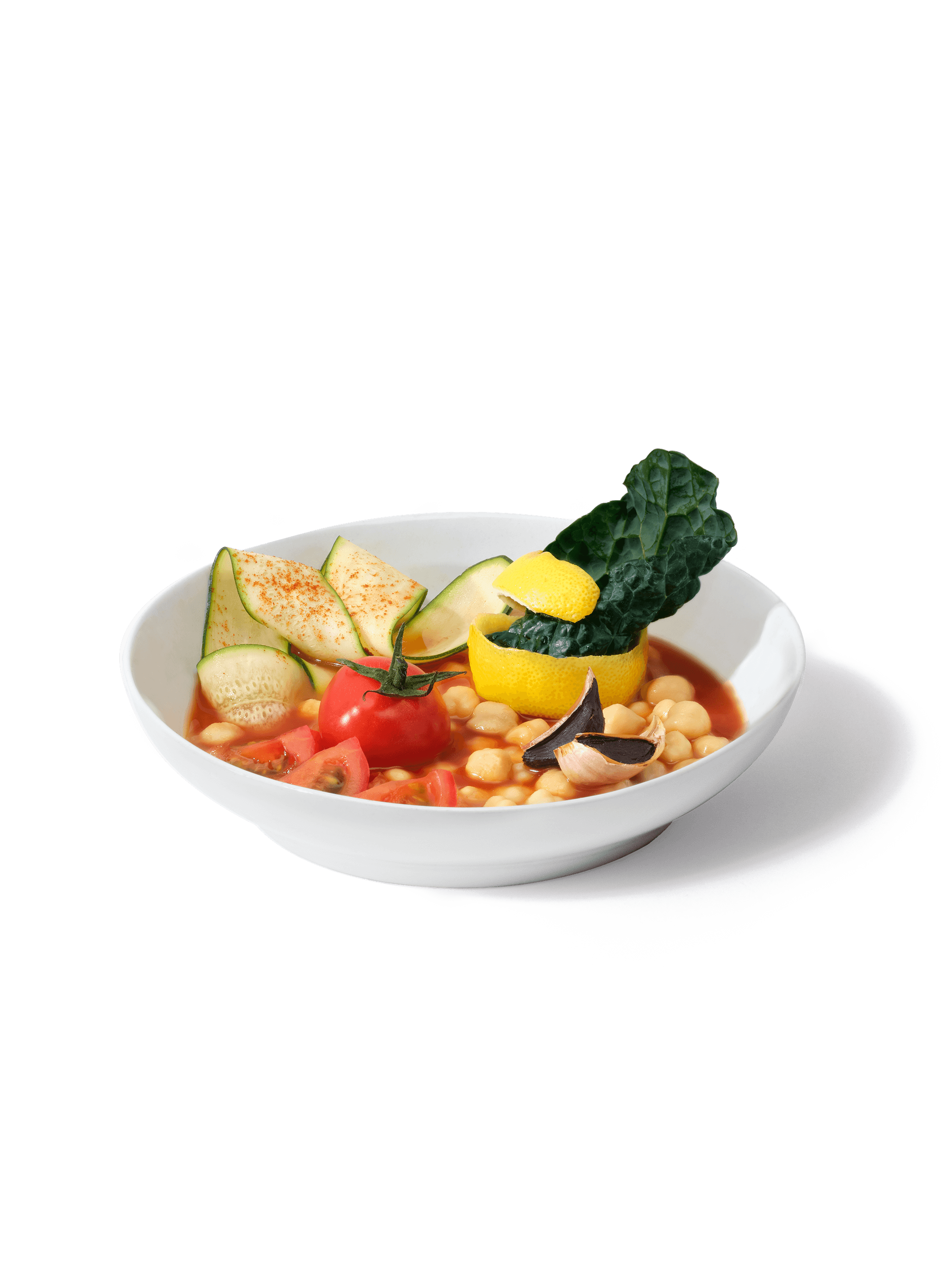 A bowl filled with ingredients included in Daily Harvest's Tomato + Zucchini Minestrone Soup, including zucchini, tomato, chickpea, kale, black garlic, and basil.
