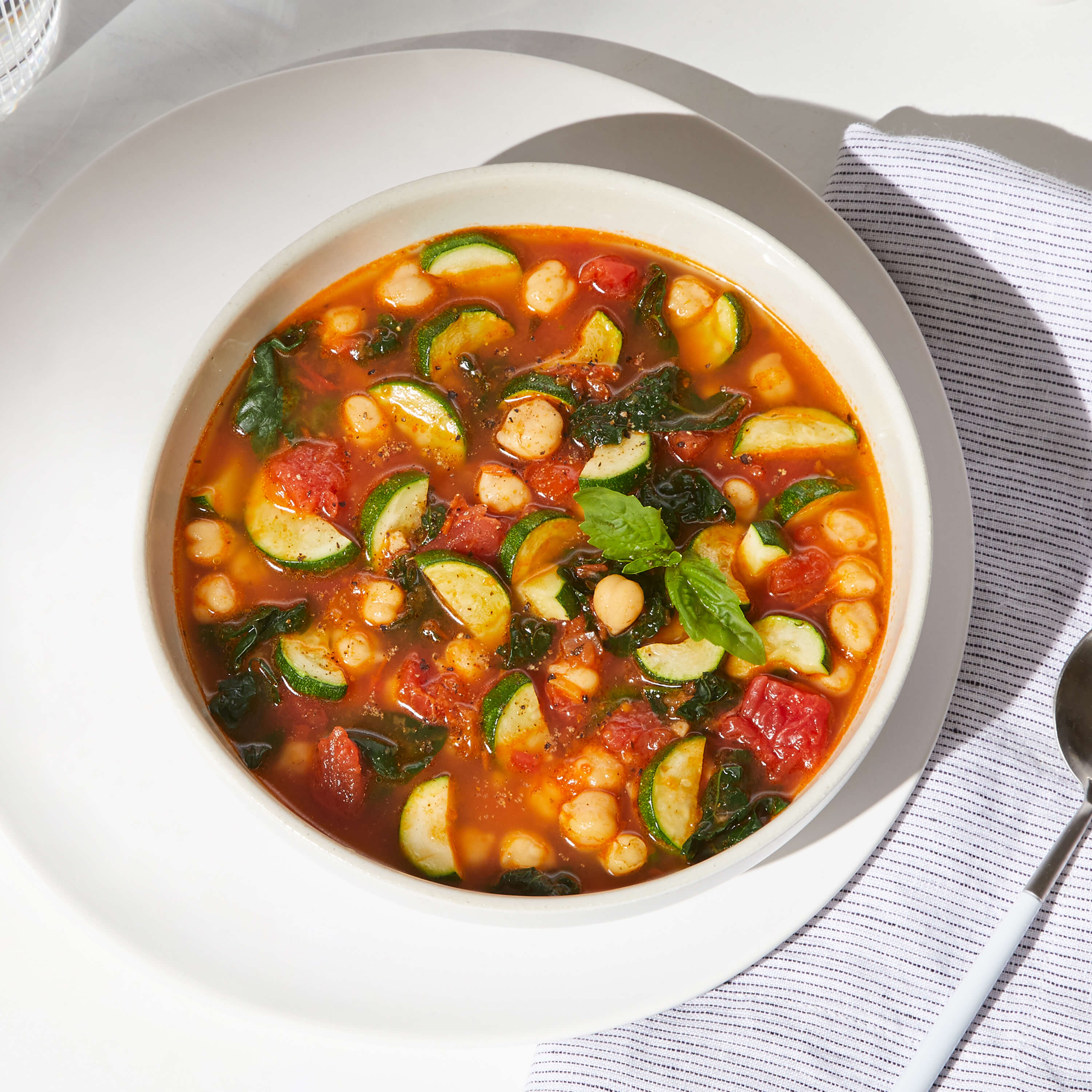 Lifestyle image of Daily Harvest Tomato + Zucchini Minestrone Soup prepared in a bowl with garnish.