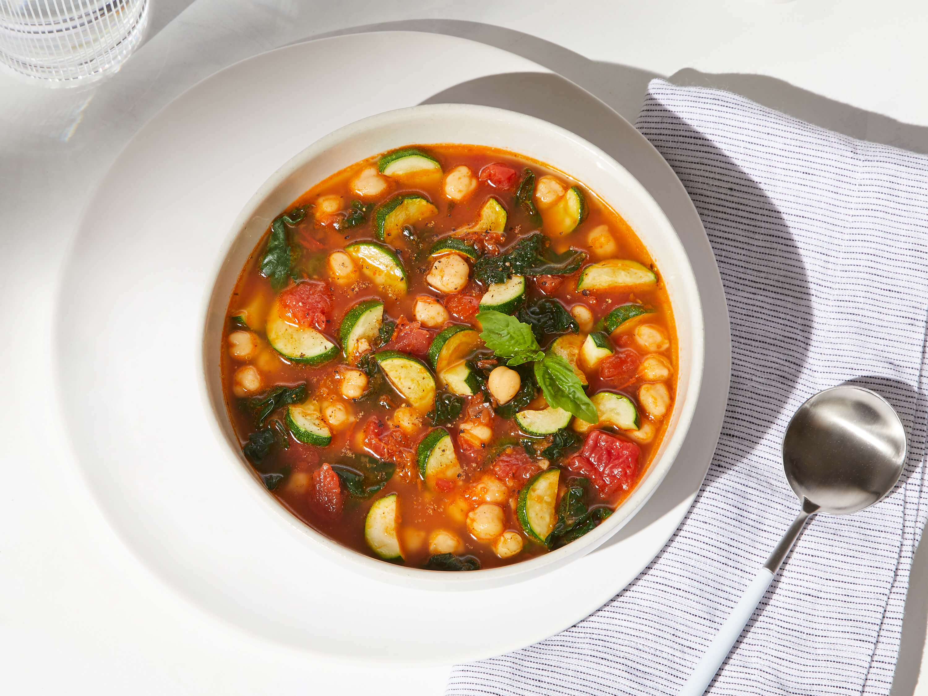 Lifestyle image of Daily Harvest Tomato + Zucchini Minestrone Soup prepared in a bowl with garnish.