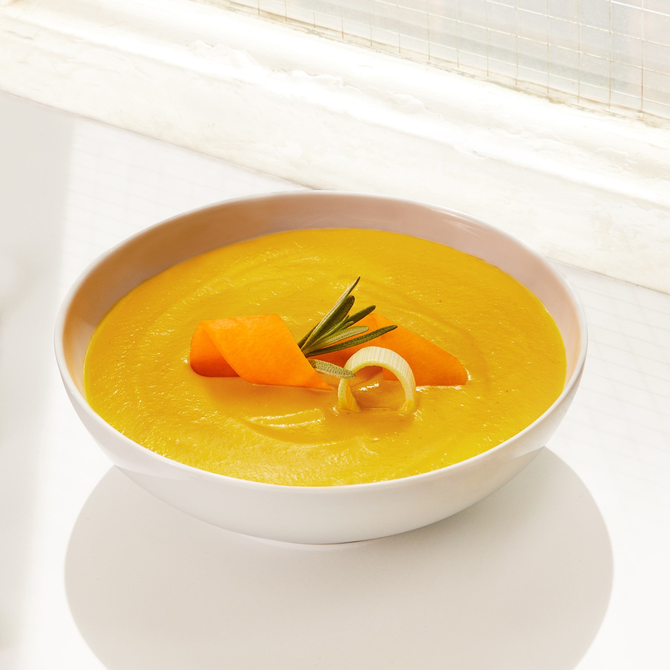 Lifestyle image of Daily Harvest Butternut Squash + Rosemary Soup prepared in a bowl with garnish.