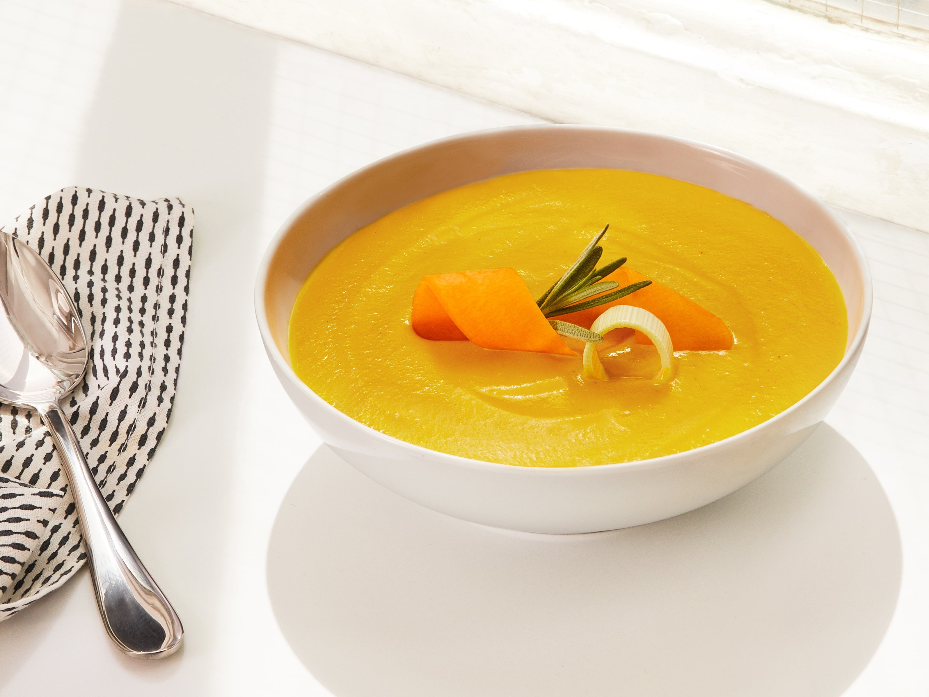 Lifestyle image of Daily Harvest Butternut Squash + Rosemary Soup prepared in a bowl with garnish.