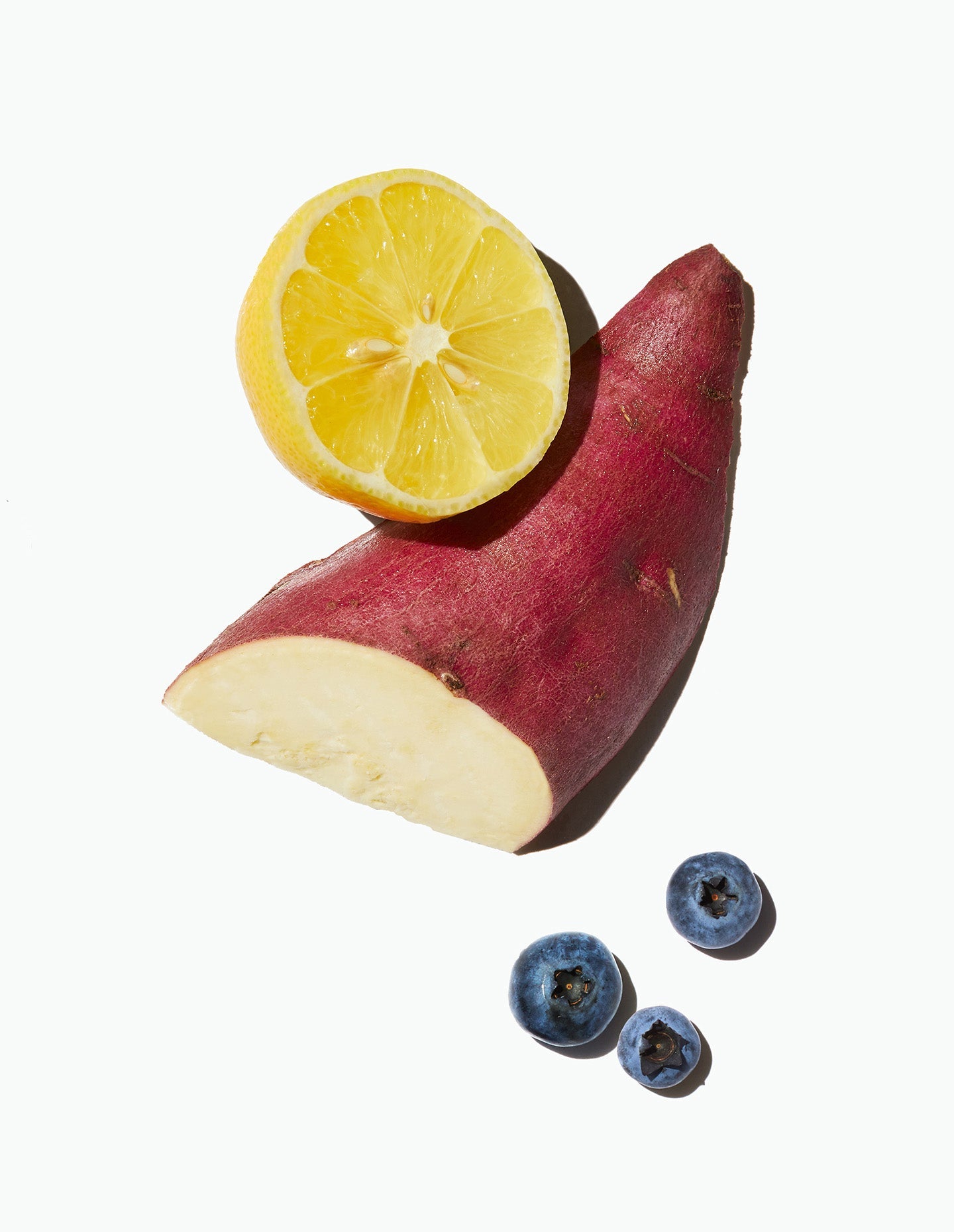 Image of Daily Harvest Blueberry + Lemon Oat Bowl ingredients, including a sliced murasaki sweet potato alongside a lemon and some blueberries.