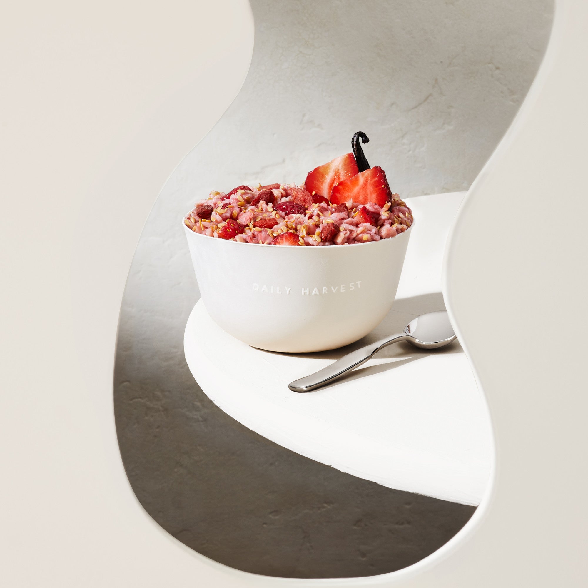 Lifestyle image of Daily Harvest Strawberry + Goji Berry Oat Bowl prepared in a bowl with a spoon and two strawberry halves on the side.