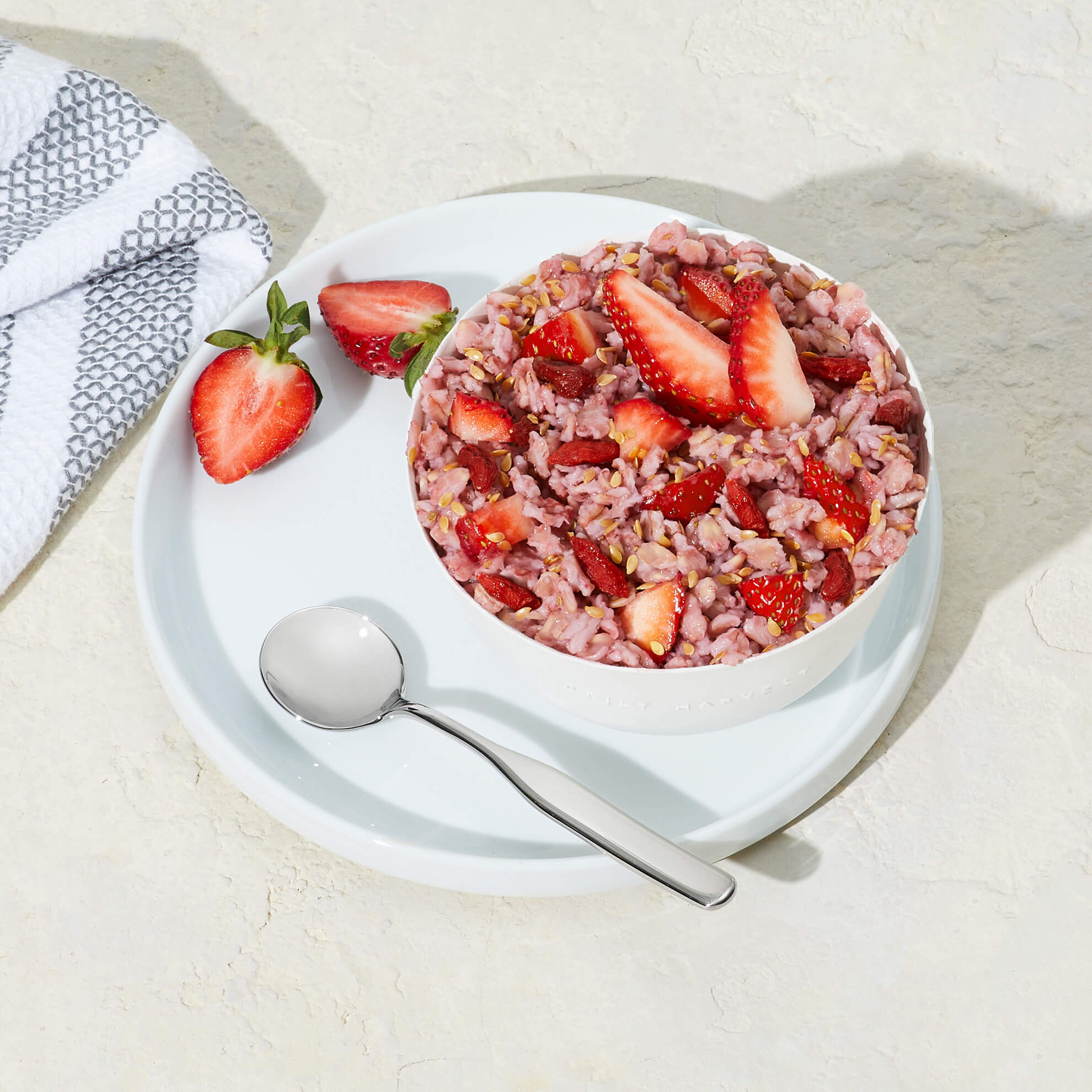 Lifestyle image of Daily Harvest Strawberry + Goji Berry Oat Bowl prepared in a bowl with a spoon and two strawberry halves on the side.