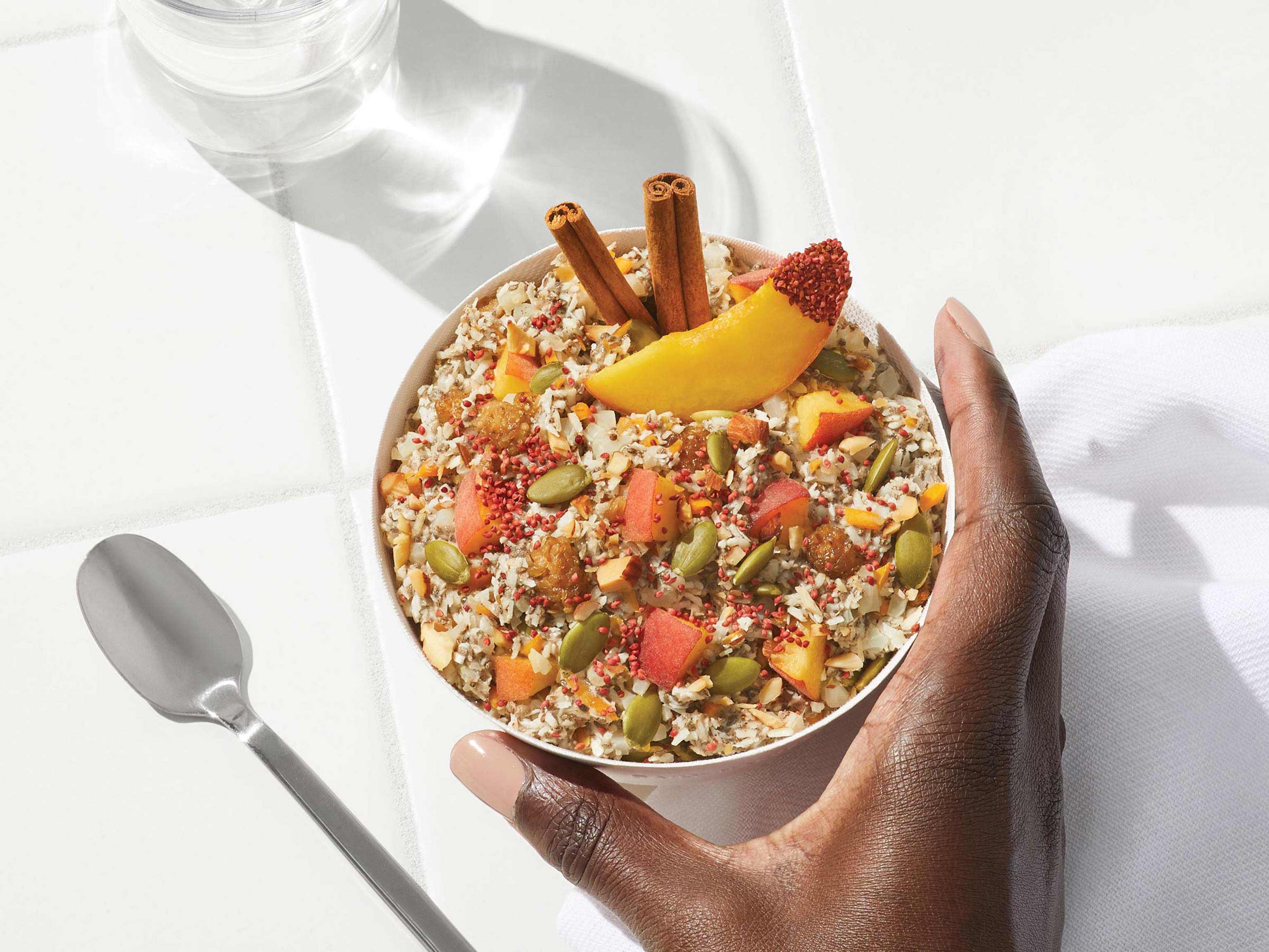 Overhead lifestyle image of Daily Harvest Peach + Cinnamon Bowl prepared in a bowl with cinnamon and peach garnish.