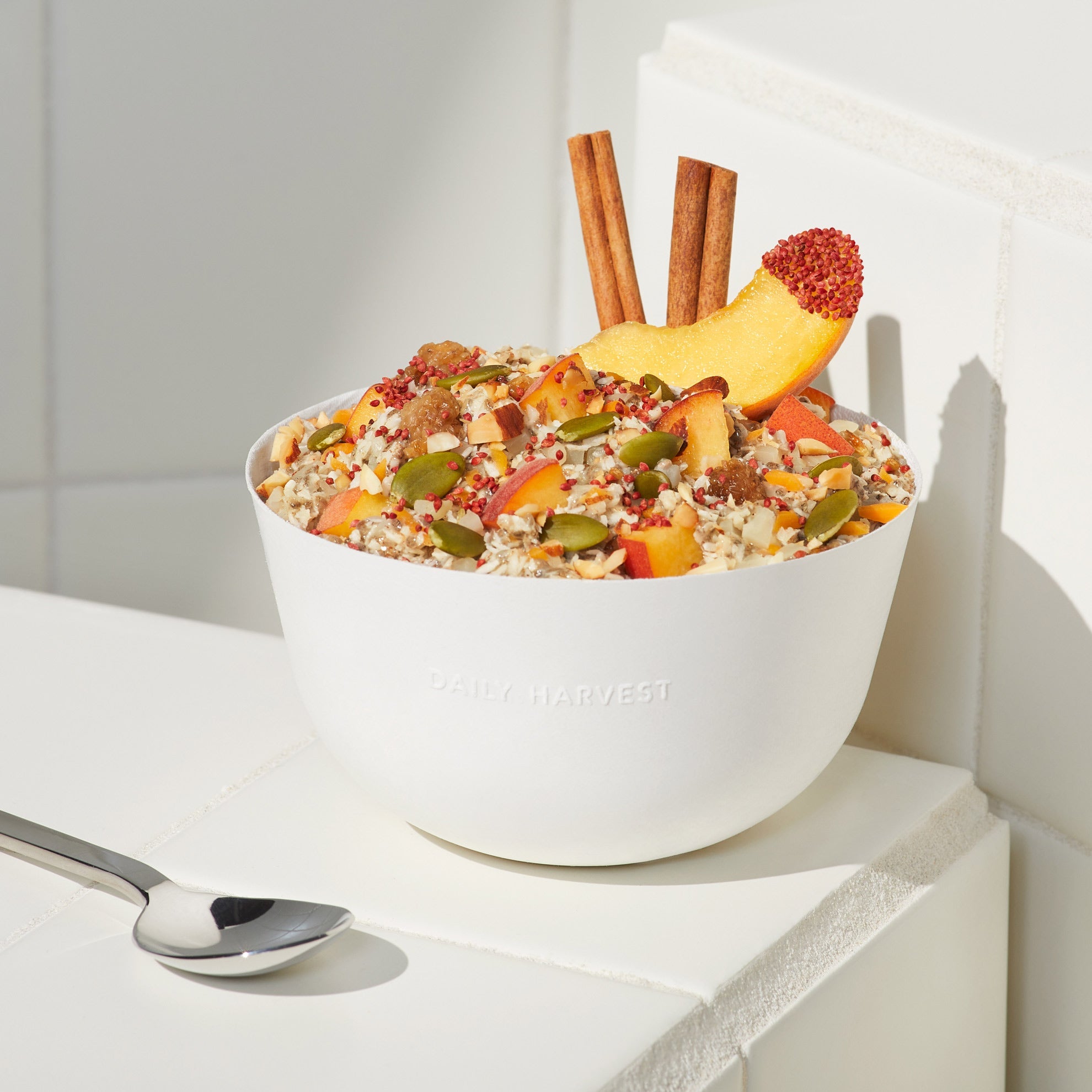 Lifestyle image of Daily Harvest Peach + Cinnamon Bowl prepared in a bowl with ingredient garnish. 