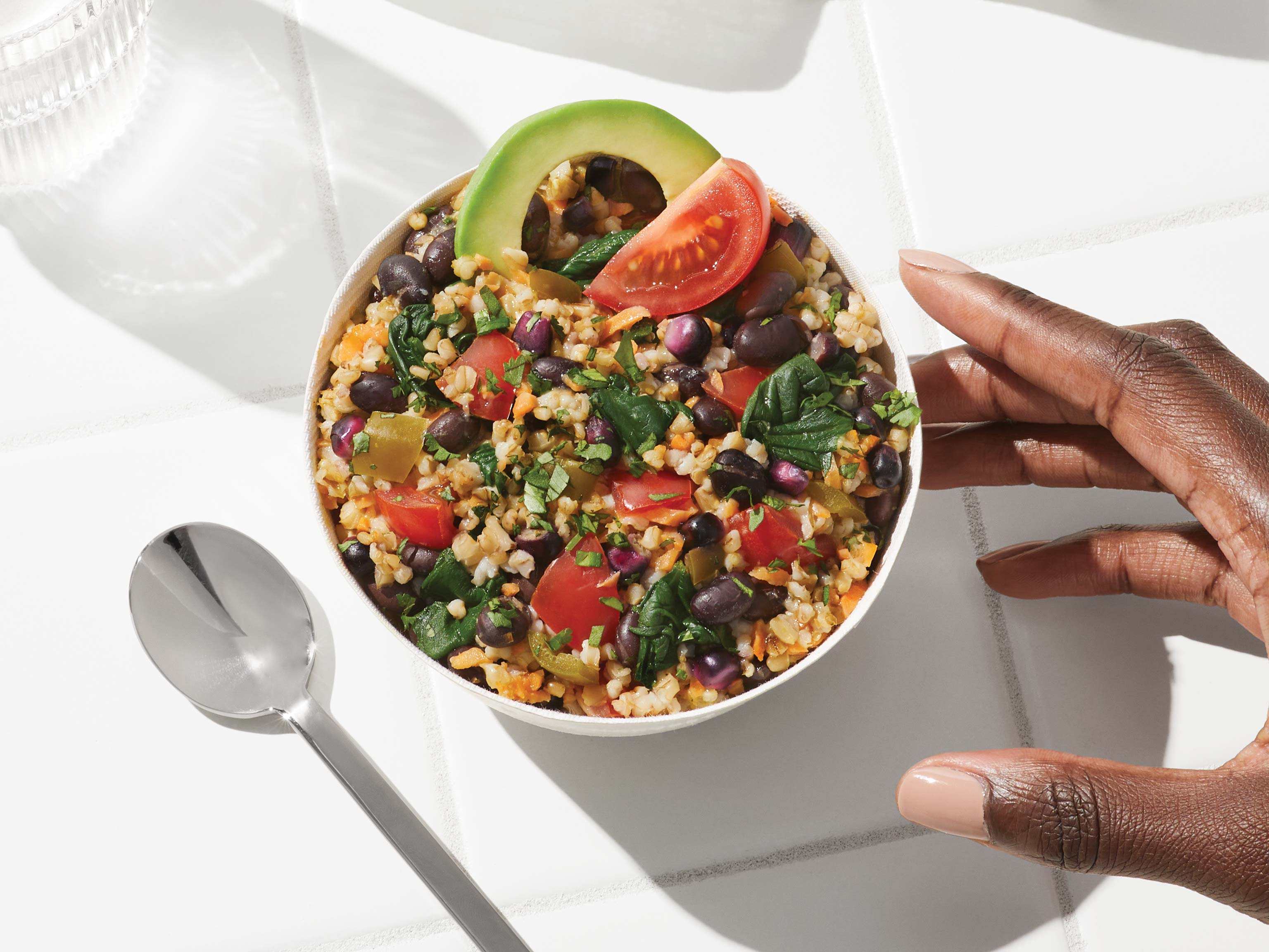 Overhead lifestyle image of Daily Harvest Black Bean + Tomatillo Oat Bowl prepared in a bowl with an avocado and tomatillo garnish.
