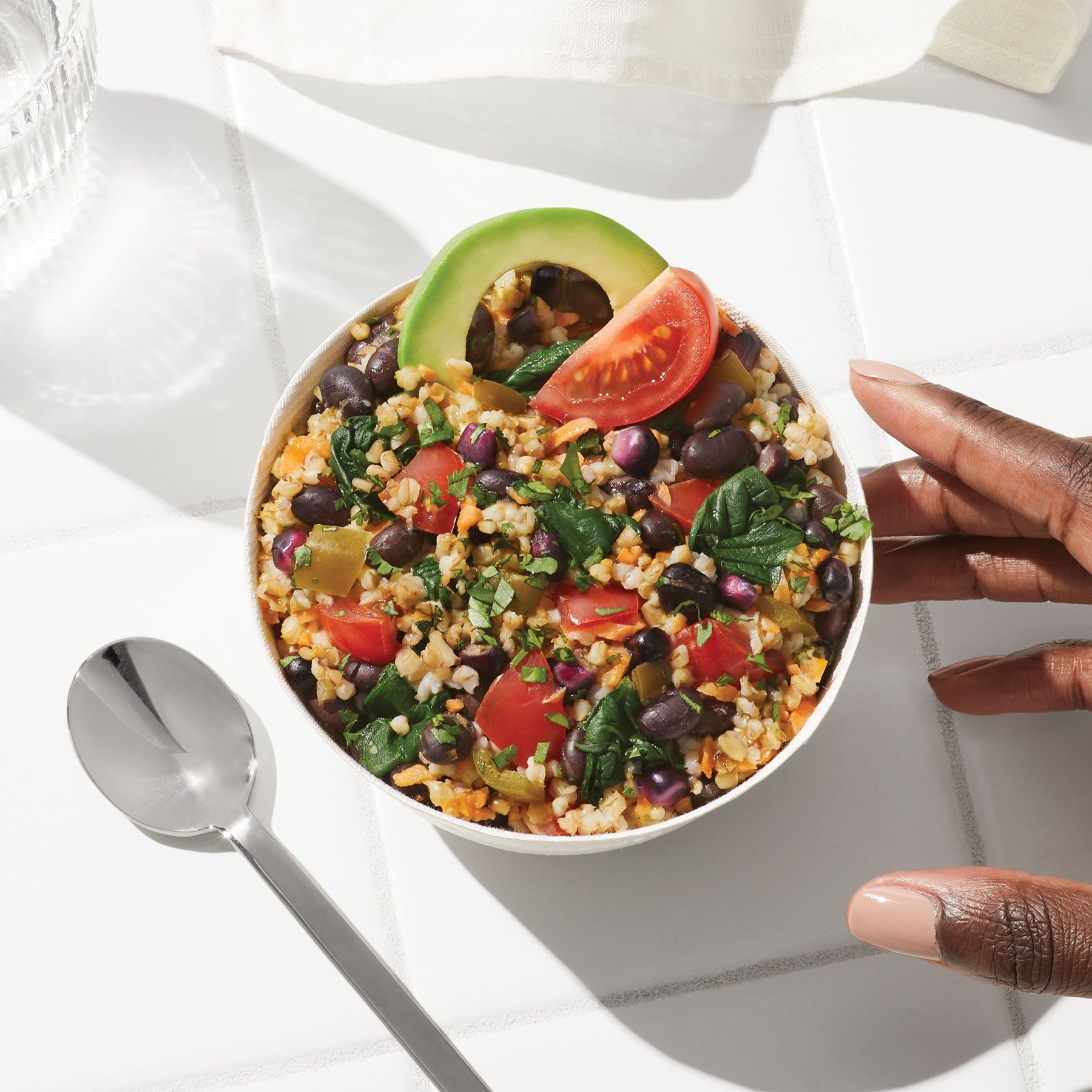 Overhead lifestyle image of Daily Harvest Black Bean + Tomatillo Oat Bowl prepared in a bowl with an avocado and tomatillo garnish.