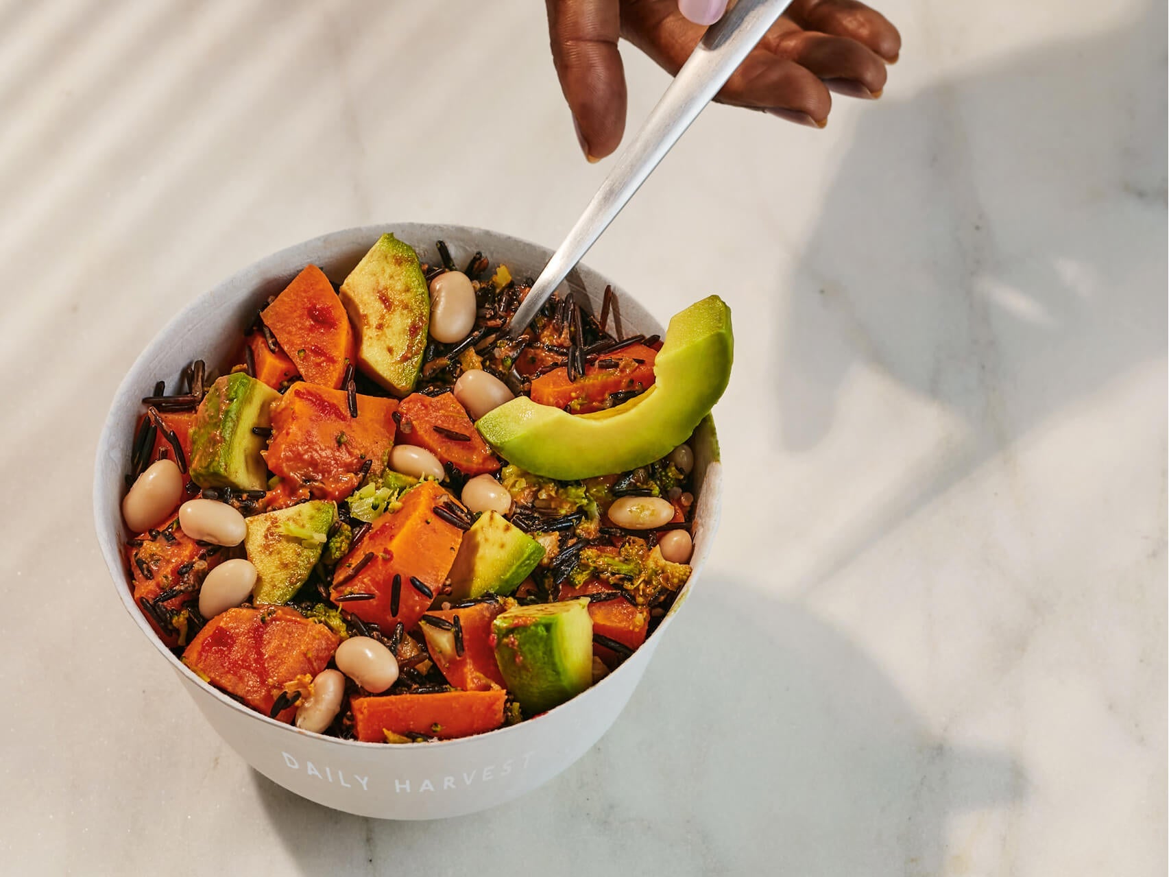 A hand scooping a bite of Sweet Potato + Wild Rice Hash onto a spoon