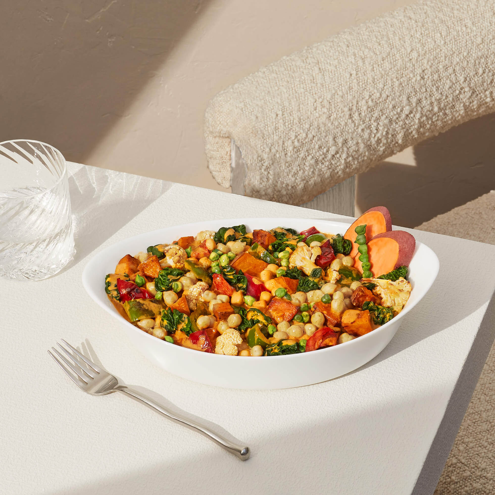 Image of a prepared coconut curry harvest bake sitting in a white bowl on a white table with fork.