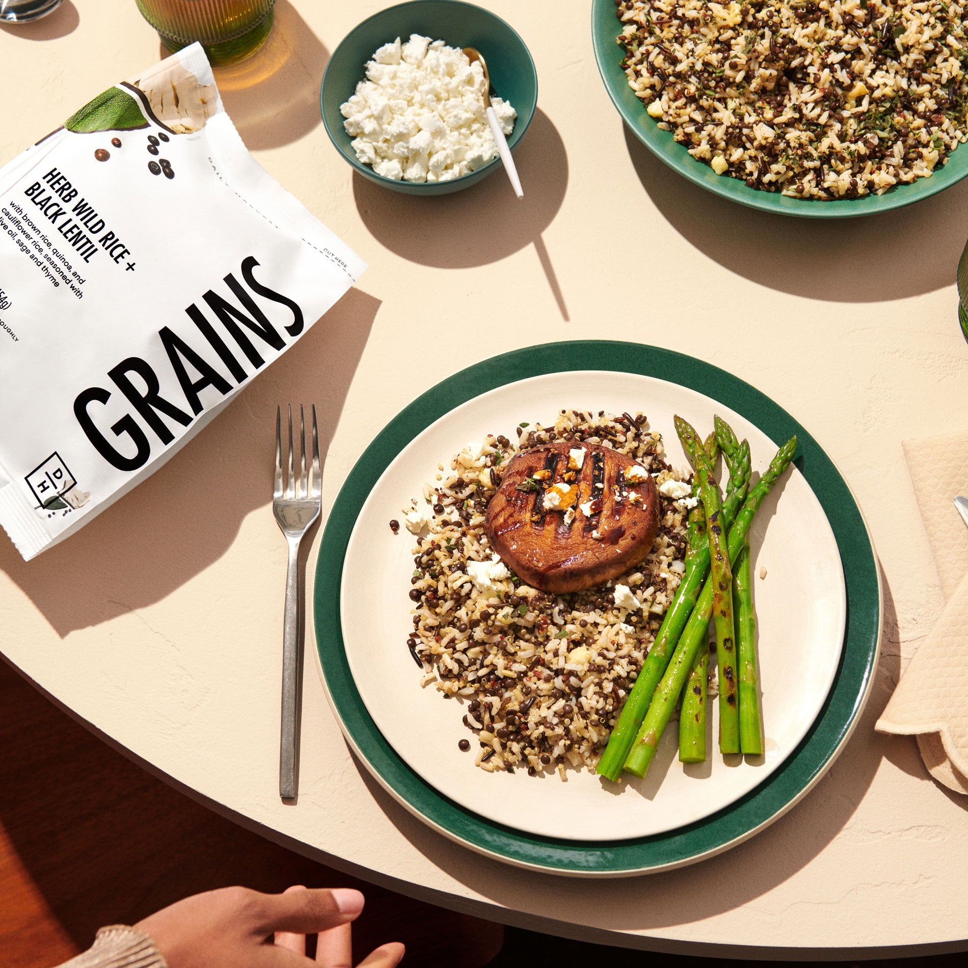 A picture of prepared Herb Wild Rice and Black Lentil grains on a plate next to asparagus on a table next to the bag of grains.