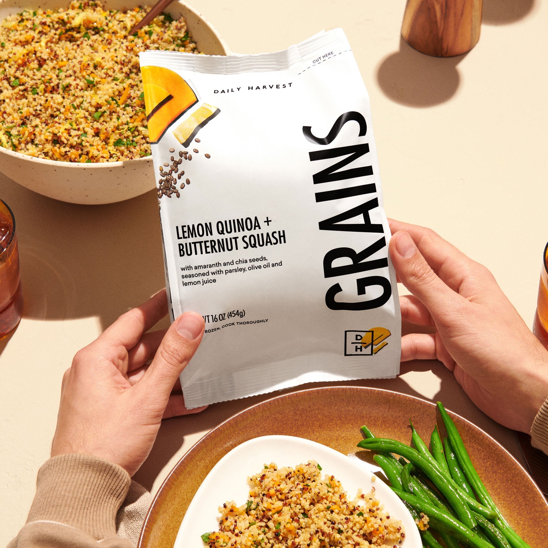 A picture of prepared Lemon Quinoa and Butternut Squash grains in a bowl on a table with a person holding the bag of grains.