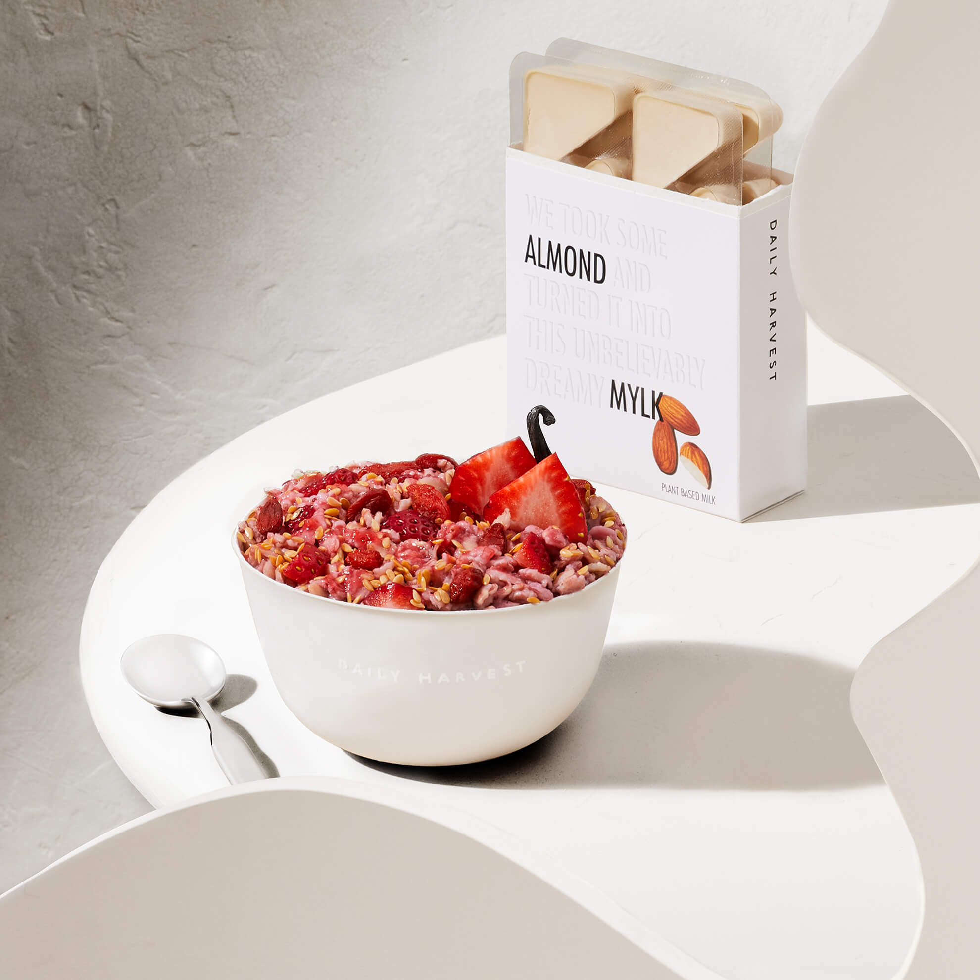 Lifestyle image of Daily Harvest Strawberry + Goji Berry Oat Bowl on table with a spoon and almond mylk on the side. 